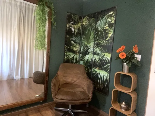 Le cabinet LeReset à Bagnols-en-Forêt : un fauteuil confortable devant un mur vert profond, un grand tableau de feuillages, un miroir et des fleurs orange.