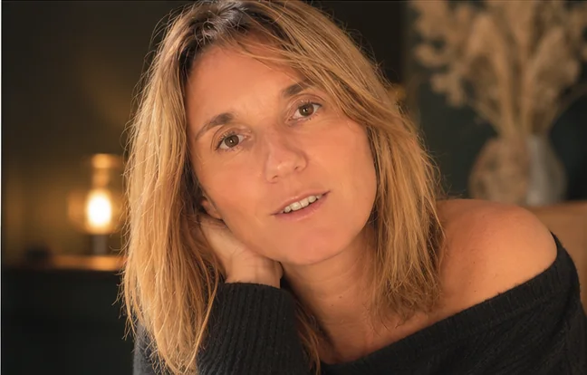 Caroline Senges en pull noir, la tête posée sur la main, dans une lumière chaude, près d'une lampe allumée.